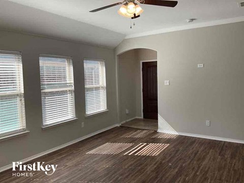 an empty living room with a ceiling fan and three windows