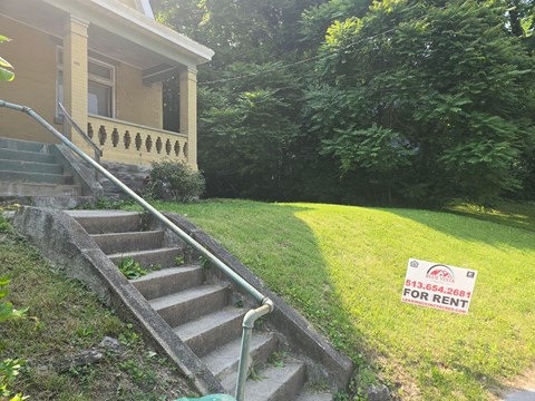 A house with a staircase and a sign that says "For Rent".