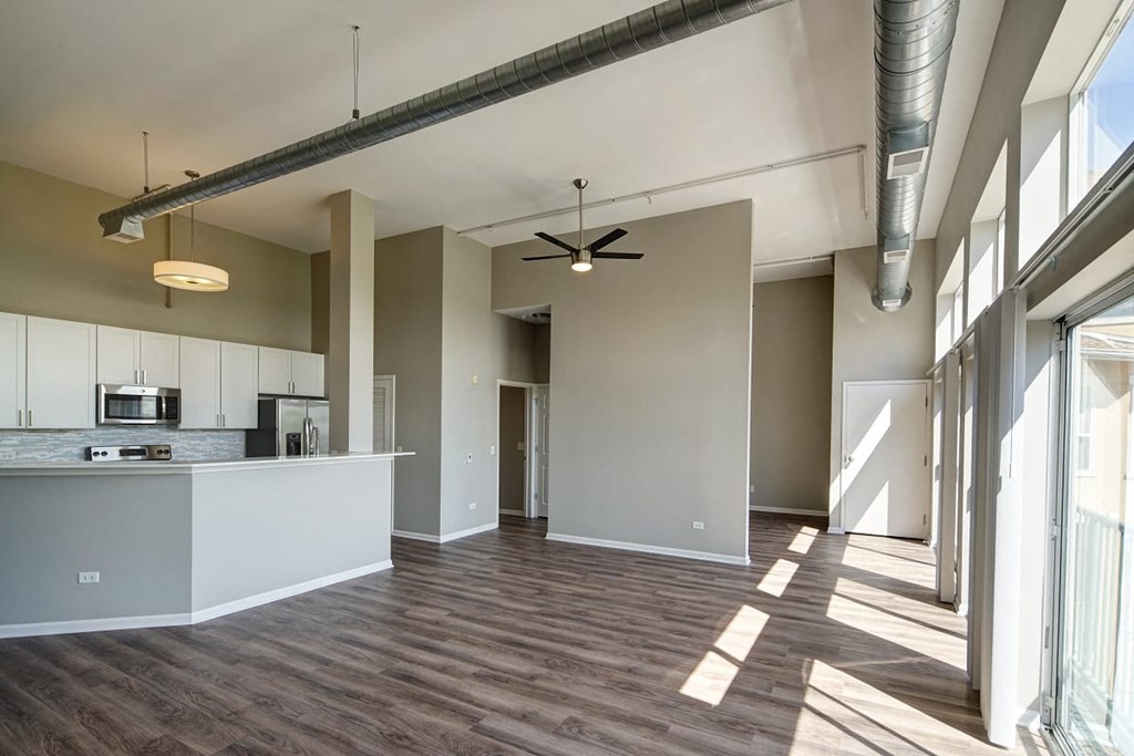 an empty living room with a kitchen and a ceiling fan