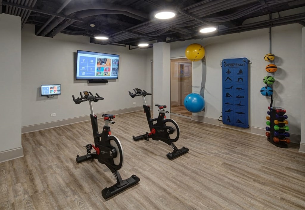a fitness room with two exercise bikes and a yellow ball on the wall