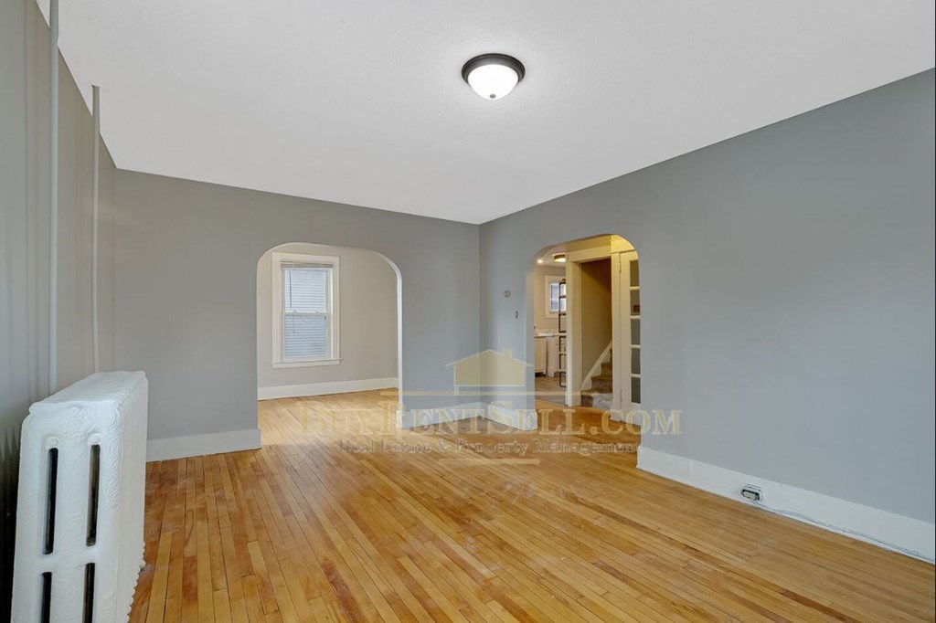 a renovated living room with a hard wood floor and an arched doorway