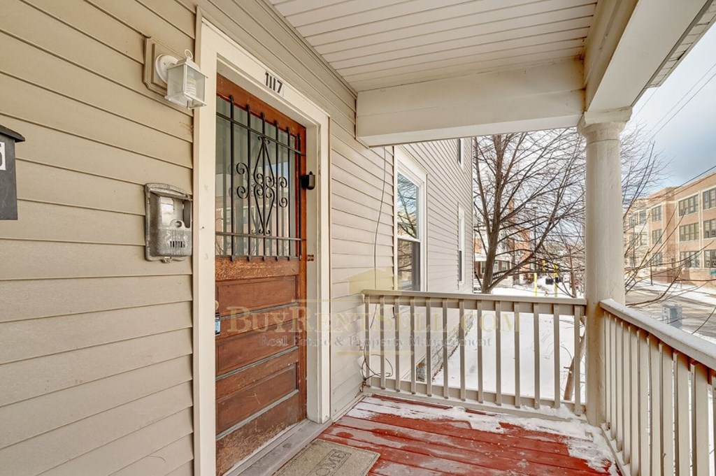 the front porch of a house with a wooden door and a white railing