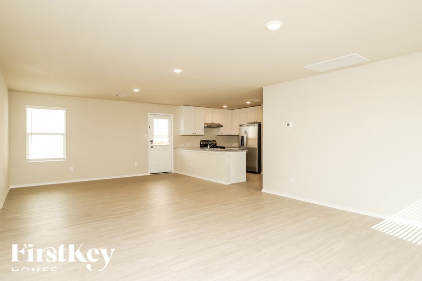 A spacious empty room with wooden flooring and a kitchen area in the background.