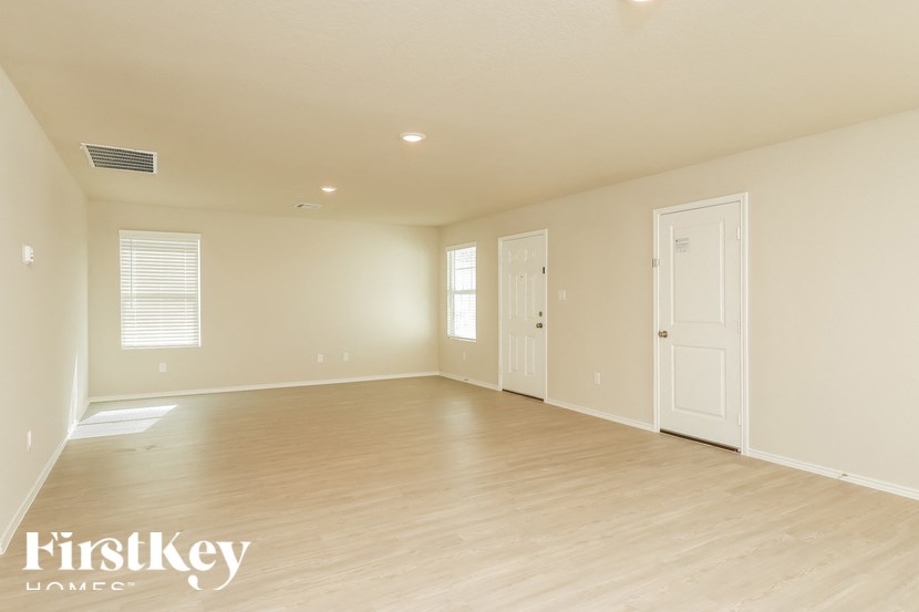 A spacious empty room with wooden flooring and white walls.