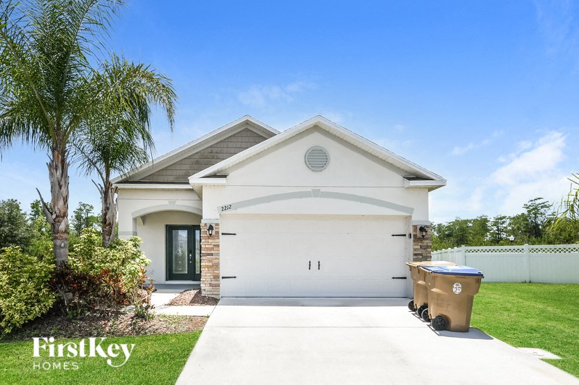 a white house with a garage door and a trash can on the driveway