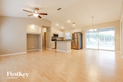 A spacious living room with a kitchen in the background and a ceiling fan in the middle of the room.