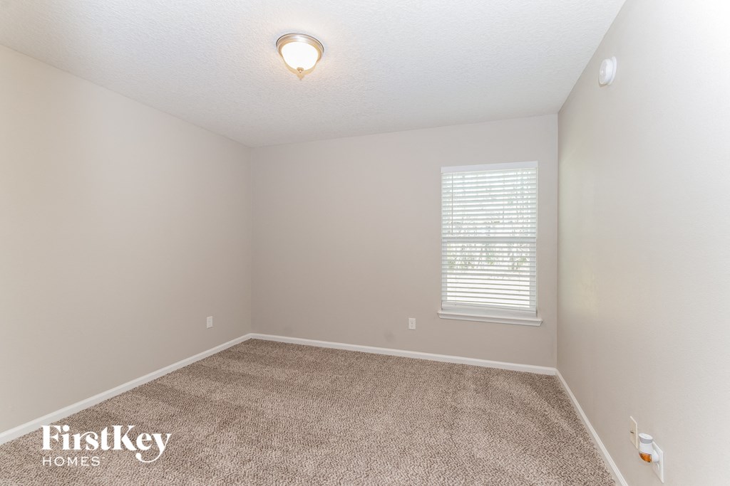 A carpeted room with a window and a light fixture on the ceiling.