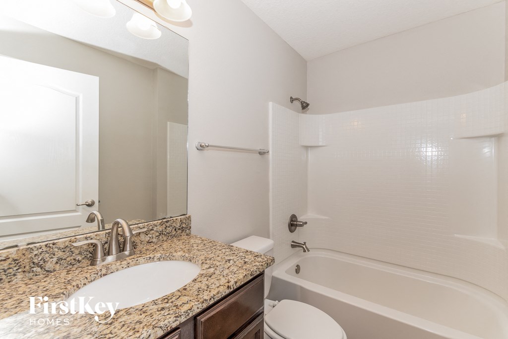 A bathroom with a granite countertop and a white tub.