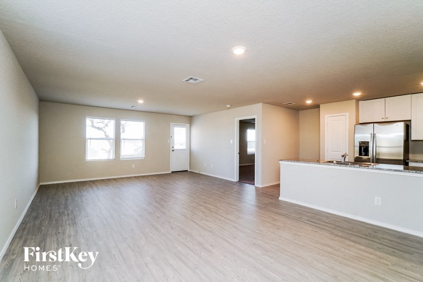 A spacious room with wooden flooring and a kitchen area with white cabinets.