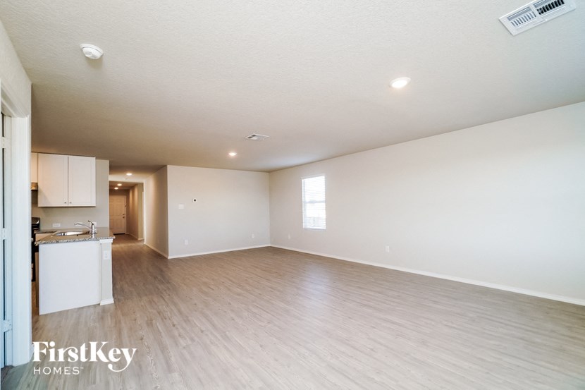 A spacious empty room with wooden flooring and a small kitchen area in the background.