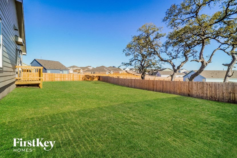 A grassy backyard with a fence and trees.