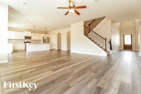 A spacious living room with wooden floors and a staircase leading to the upper level.