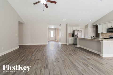 A spacious kitchen and living room with wooden floors and a ceiling fan.