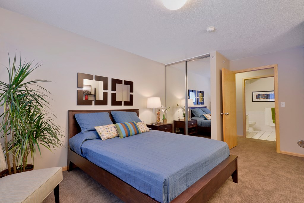 A bedroom with a bed, nightstand, and a plant.