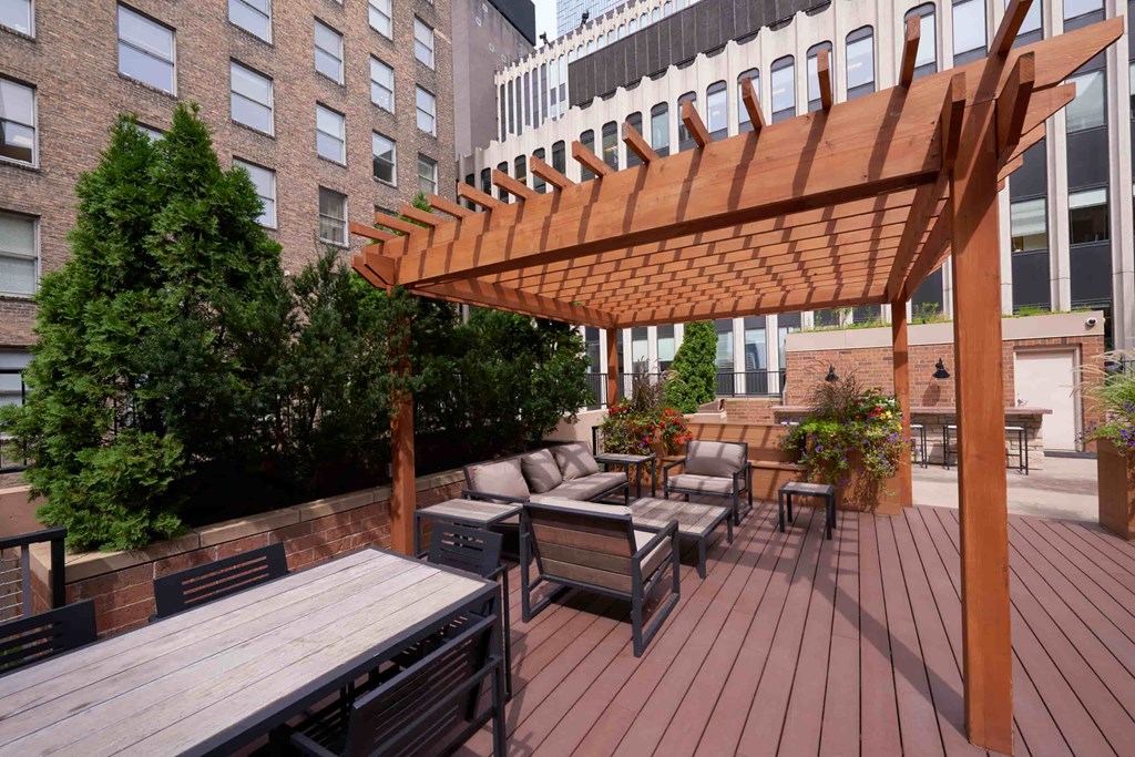 A wooden pergola over a table with chairs on a wooden deck.