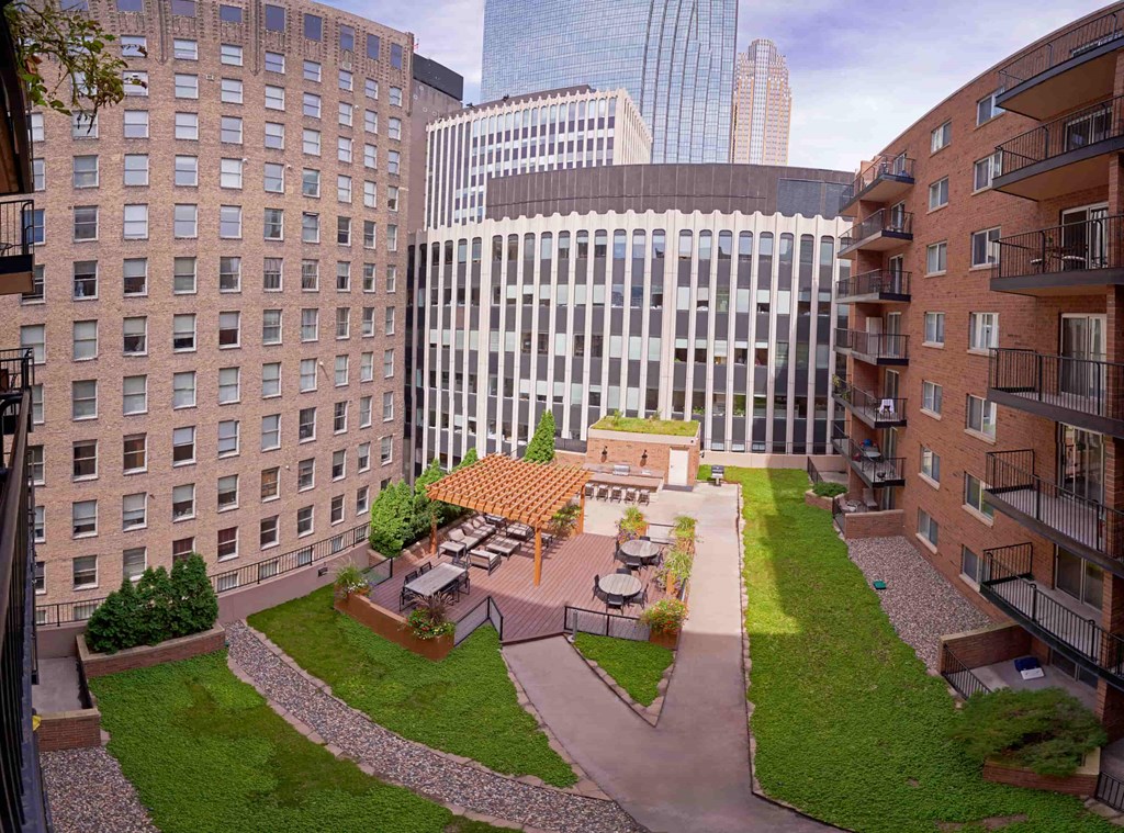 A courtyard surrounded by buildings with a furnished wooden deck in the middle and a wooden pergola over the deck.