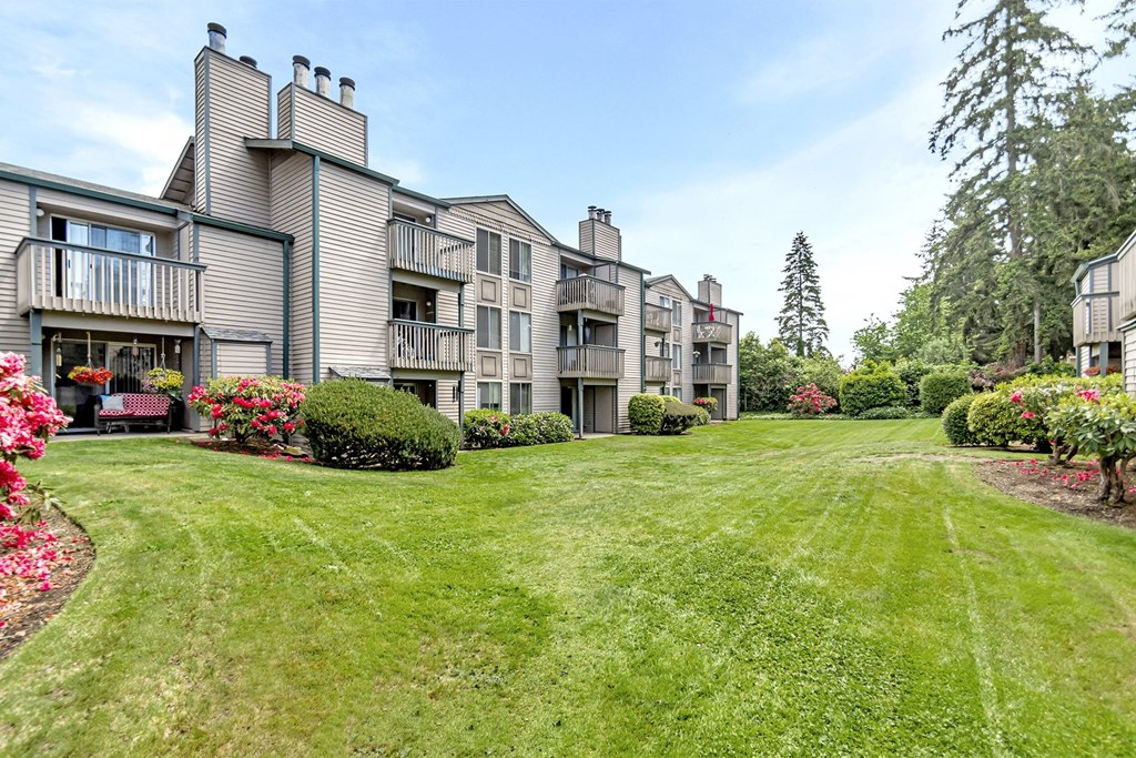 the view of an apartment building with a green lawn and flowers