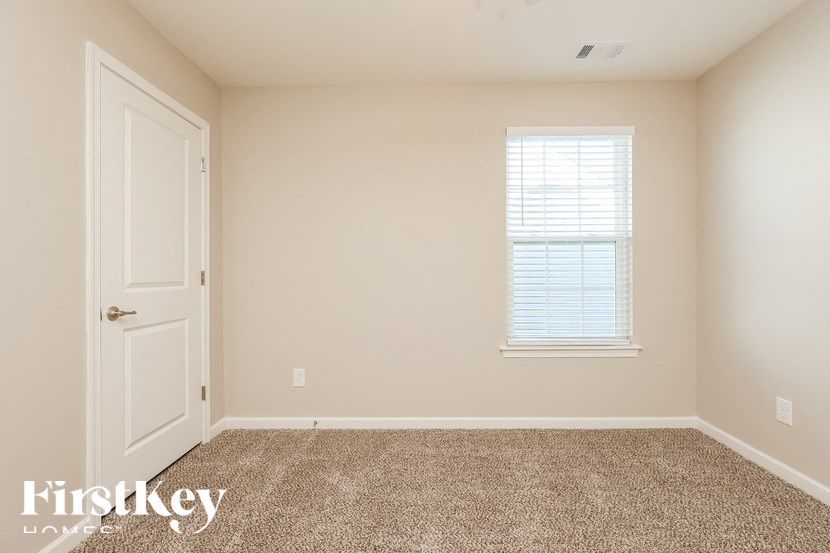 A room with a carpeted floor, a door, and a window with blinds.