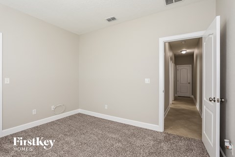 the living room of an apartment with carpet and a hallway to the bedroom