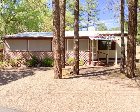 A house with a brown roof and white walls is surrounded by trees.