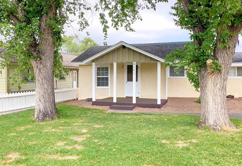 A small house with a porch is surrounded by trees.