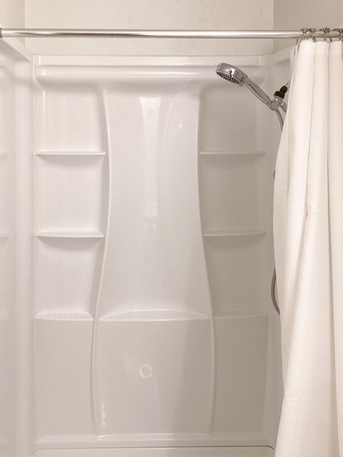 A white shower curtain is hanging in a white tiled shower.