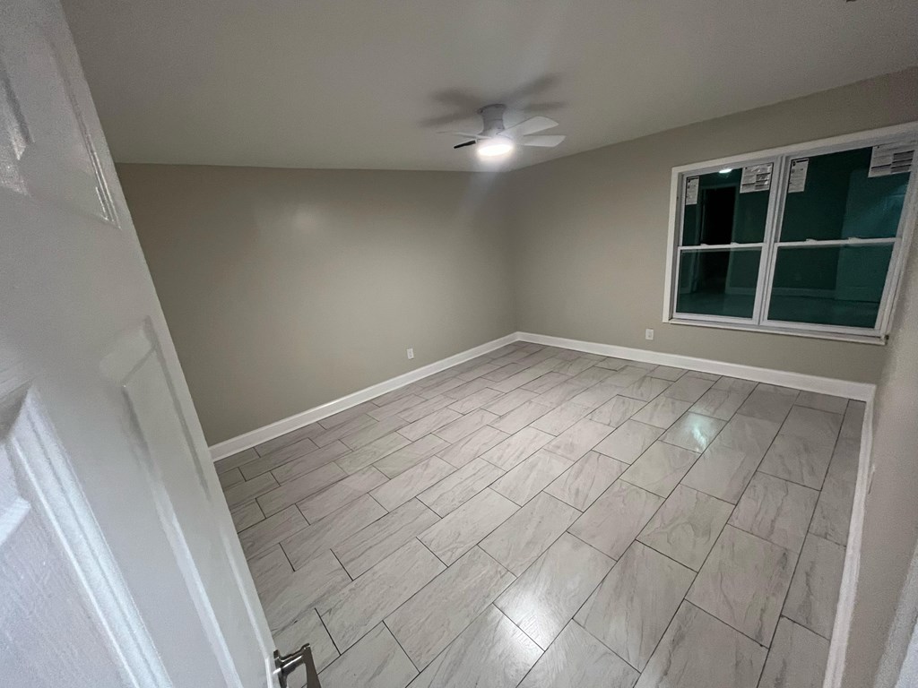 A room with a ceiling fan and a window with a view of a green area.