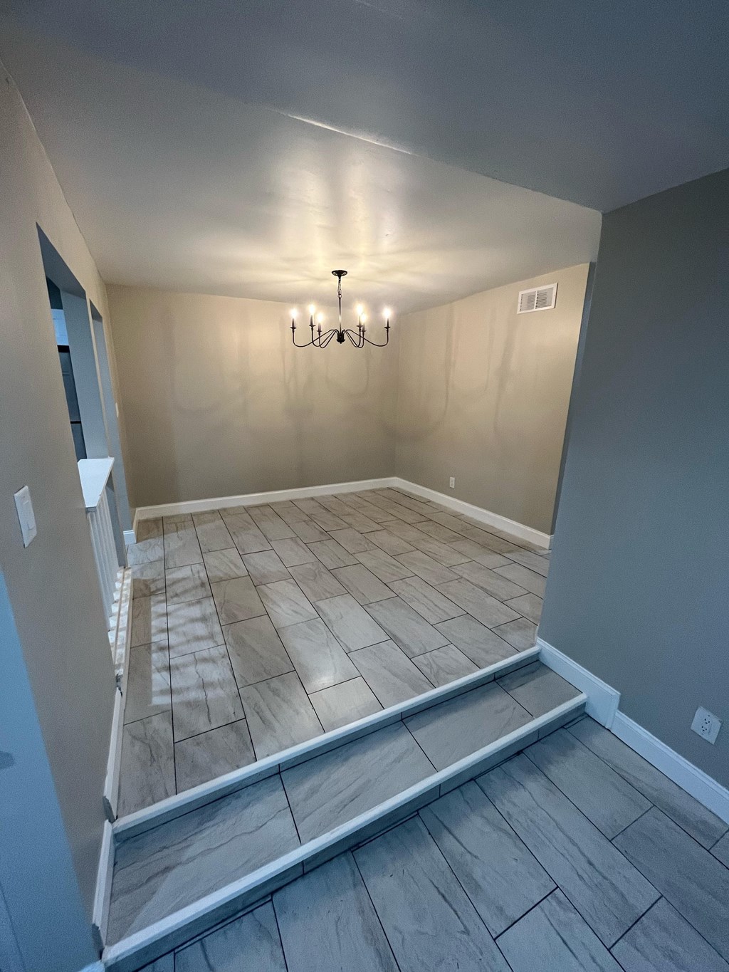 A room with a chandelier and tiled flooring.
