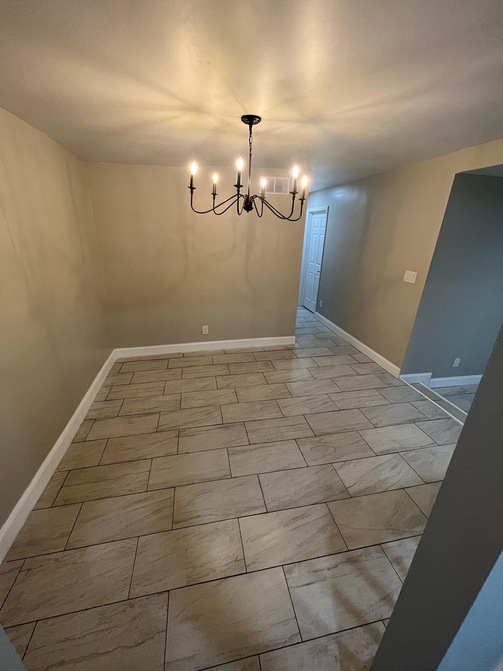 A room with a chandelier and stone tile flooring.