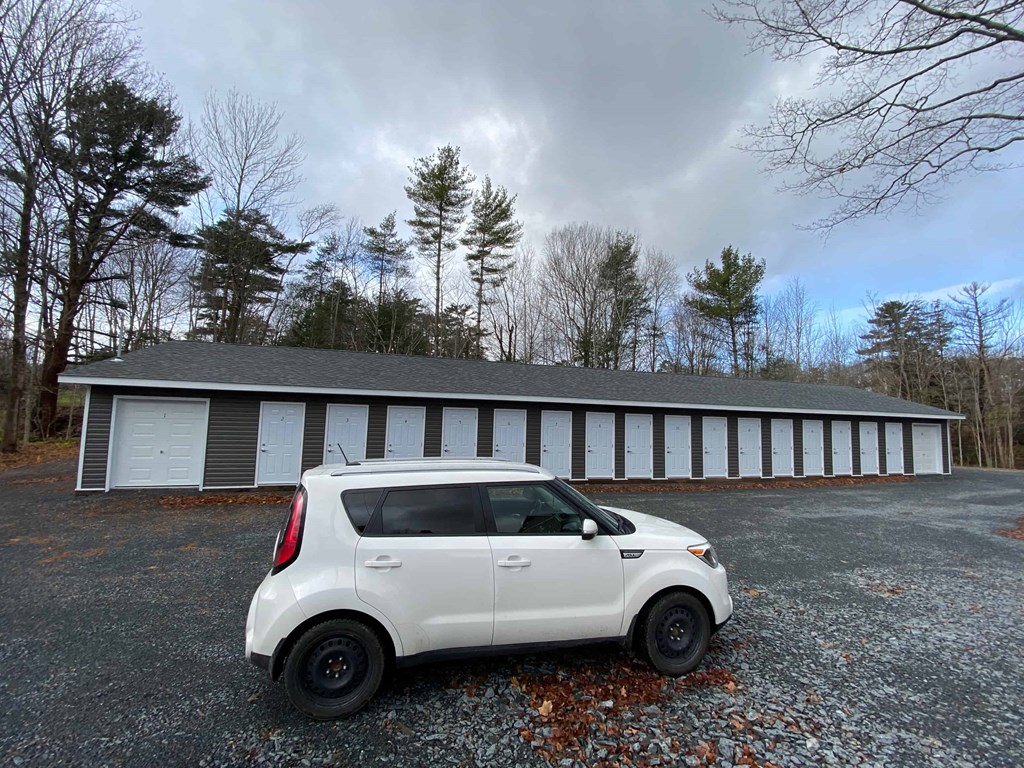 A white car is parked in front of a grey building with white doors.