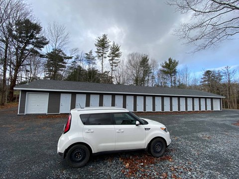 A white car is parked in front of a grey building with white doors.