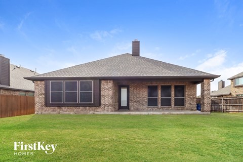 A house with a brown roof and a chimney is surrounded by a grassy lawn.