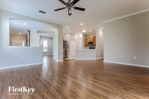 an empty living room with a ceiling fan and a kitchen