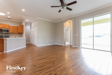 an empty living room and kitchen with wood floors and a ceiling fan