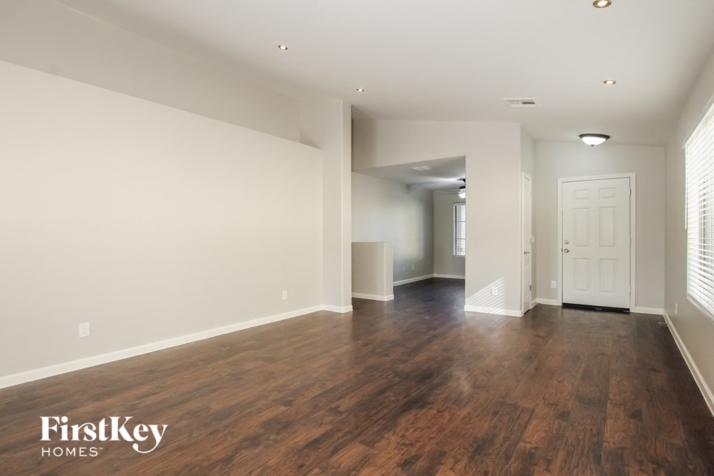 A spacious room with wooden floors and white walls, with a door on the right side.