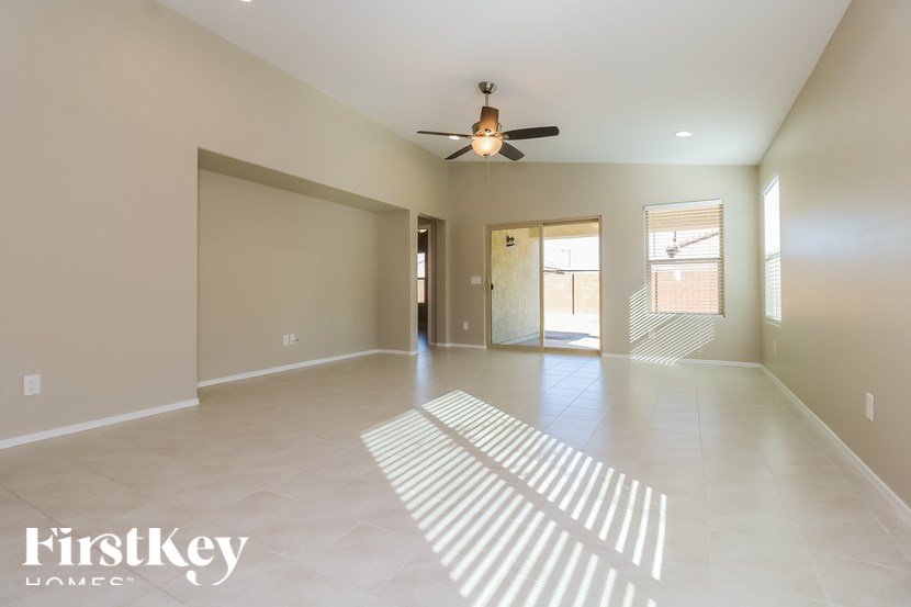 A spacious empty room with a ceiling fan and sunlight streaming in through the door.
