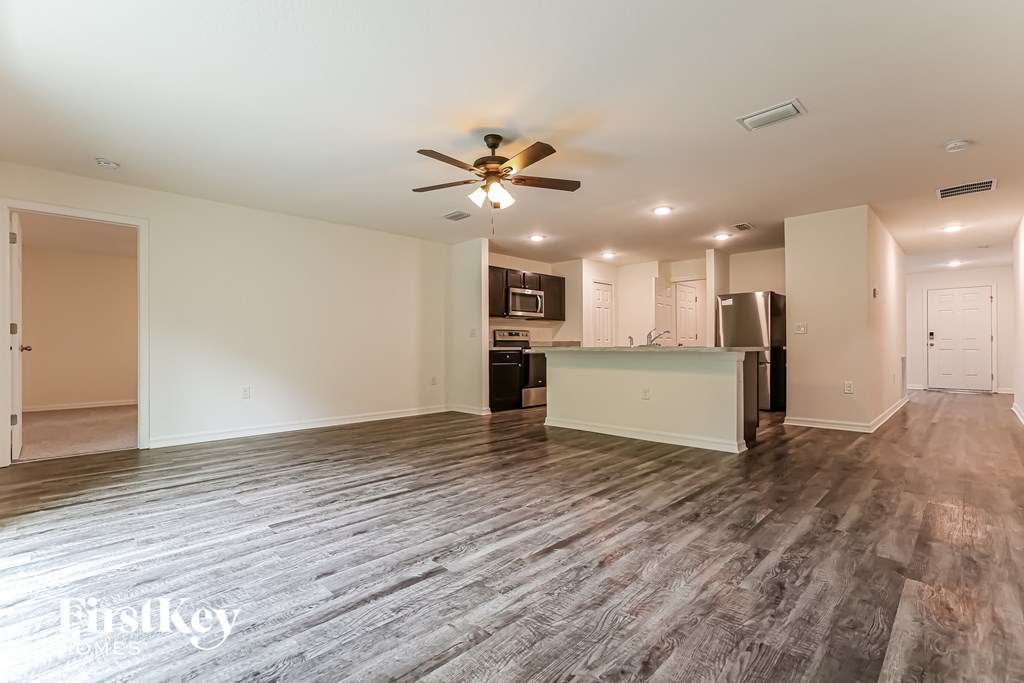 an empty living room with a ceiling fan and a kitchen