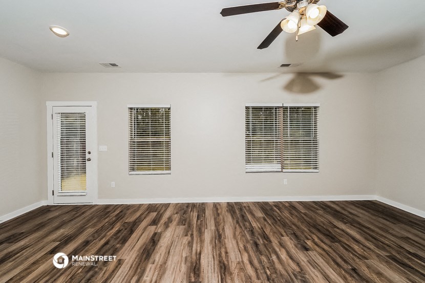 an empty living room with a ceiling fan and windows