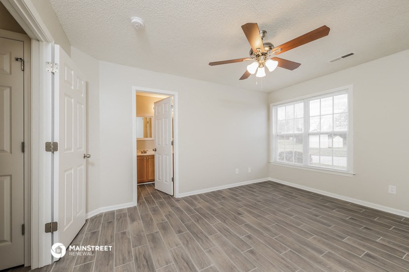 an empty living room with a ceiling fan and a door to a kitchen
