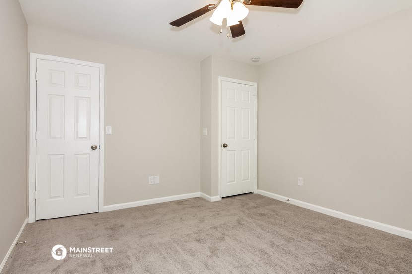 the spacious living room with two doors and a ceiling fan