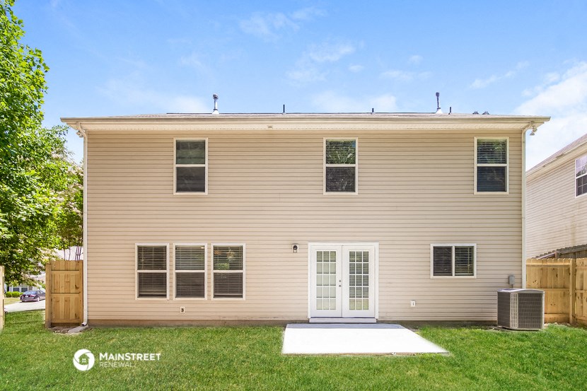 front view of a tan house with a white front door and grass