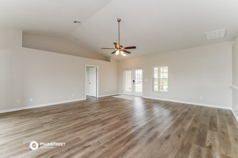 the spacious living room with hardwood flooring and a ceiling fan