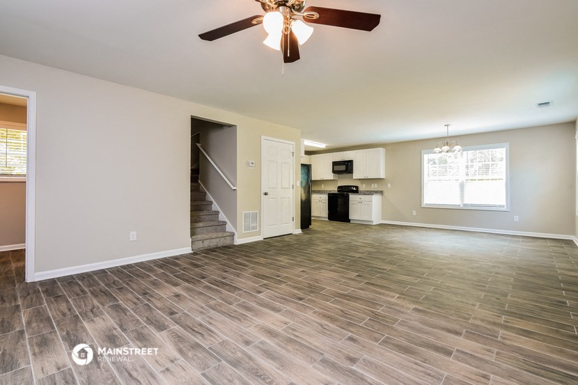an empty living room with a ceiling fan and a kitchen