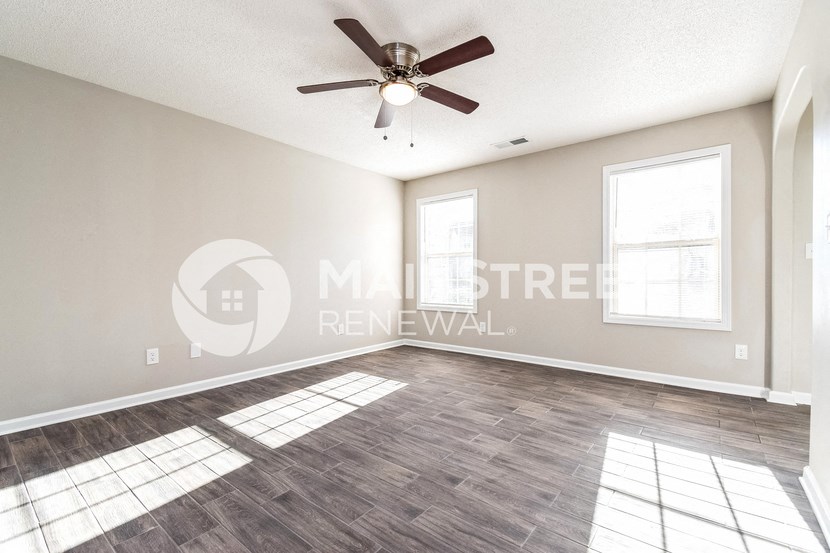 an empty living room with a ceiling fan and two windows