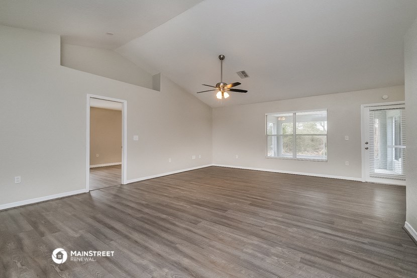 the spacious living room with wood flooring and a ceiling fan