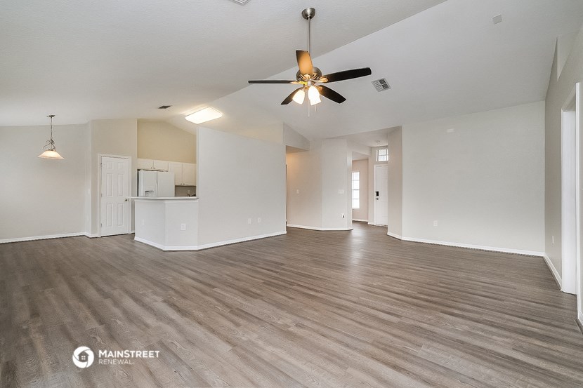 an empty living room with a ceiling fan and a kitchen