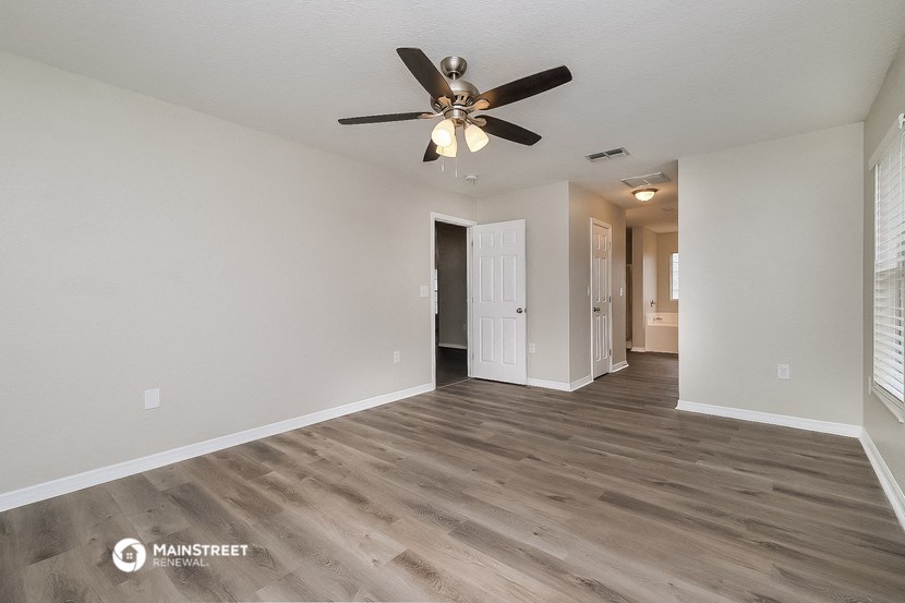 the spacious living room with a ceiling fan and white walls