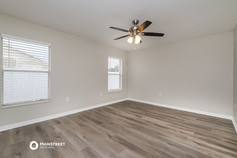 the spacious living room with wood flooring and a ceiling fan