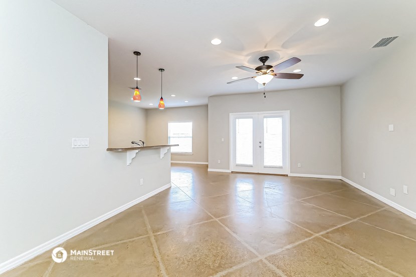 an empty living room with a ceiling fan and a kitchen