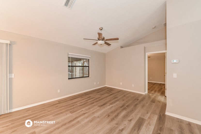 the spacious living room with wood flooring and a ceiling fan